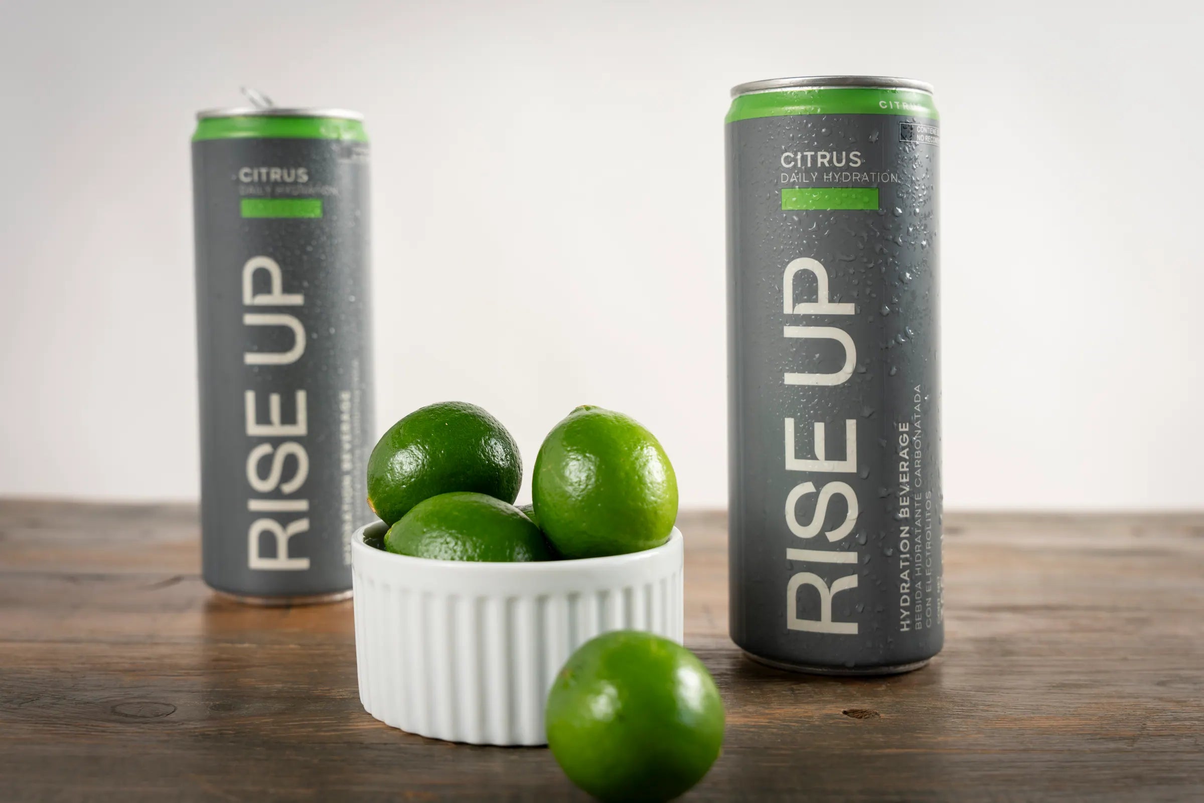 Latas de Rise Up Citrus junto a limones sobre una mesa de madera
